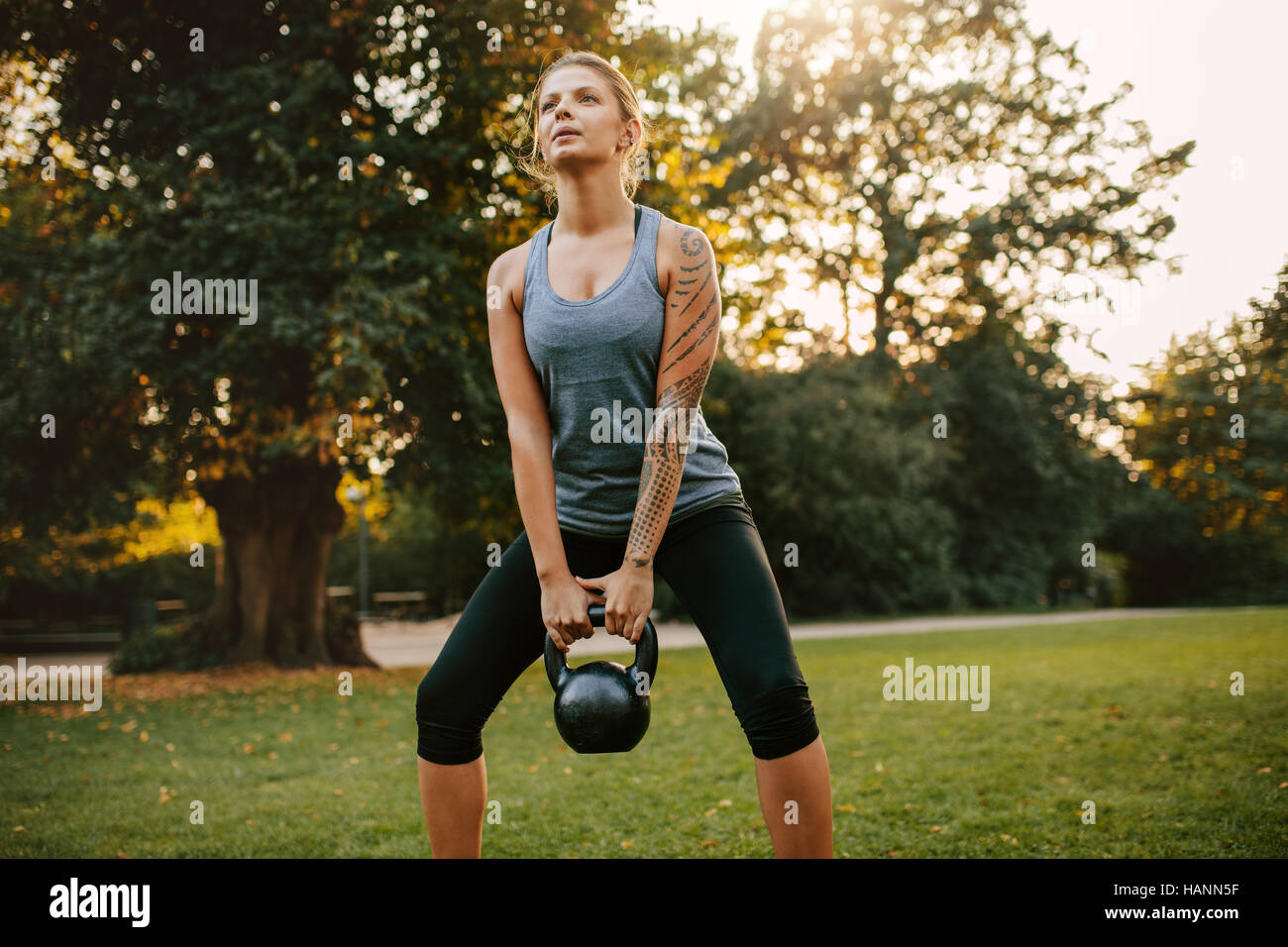 Portrait of strong young woman exercising with kettlebell weights in the park.  Fit and muscular woman training at city park in morning. Stock Photo