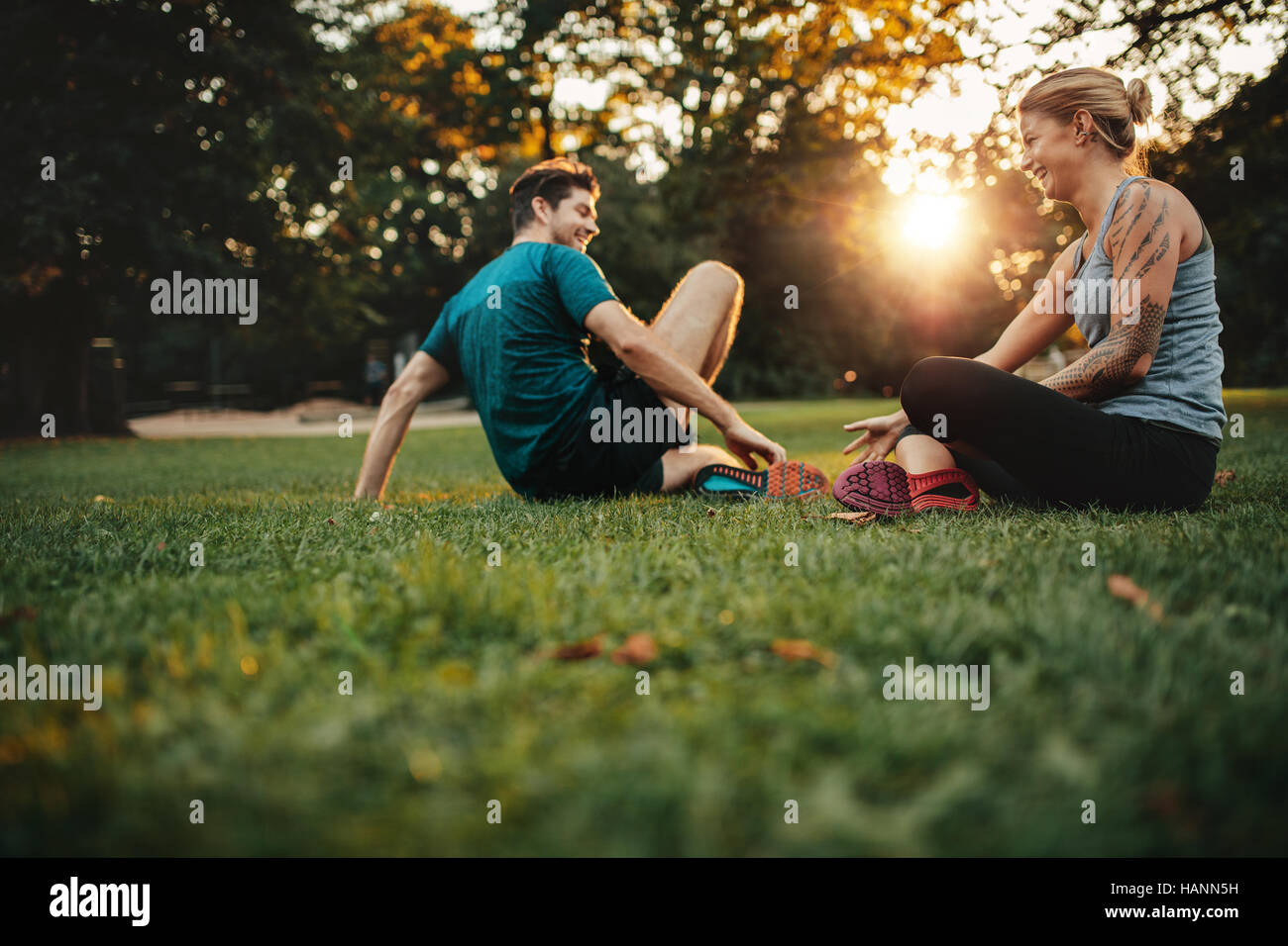 Happy fit young couple exercising in park. Relaxing after physical training session. Stock Photo