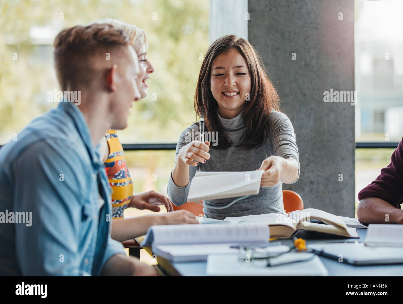 Young people sitting at table sharing notes for school assignment. Group of students studying together in a library. Stock Photo