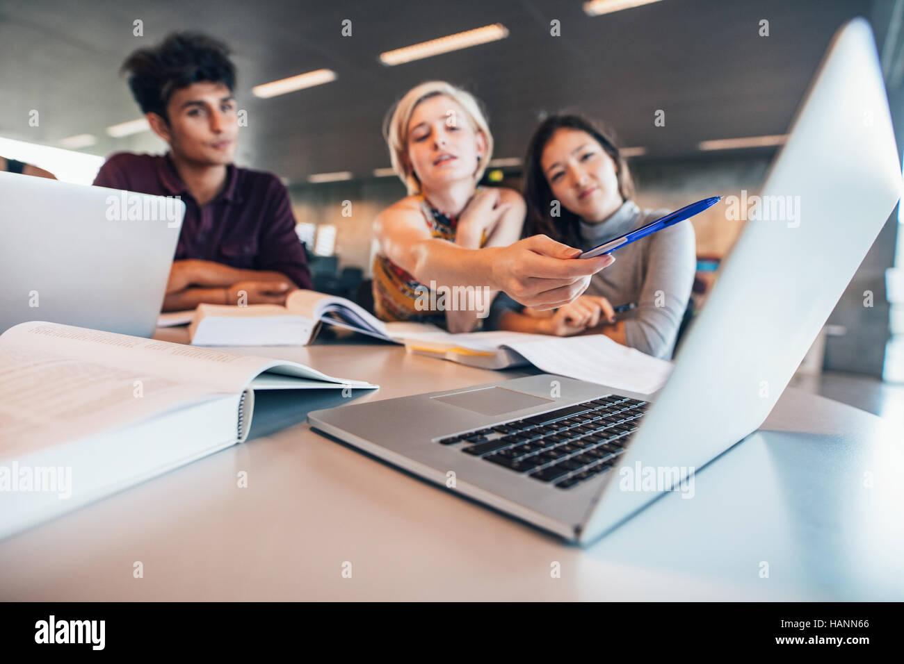 Multiracial young people doing group study at table with woman pointing at laptop. University students researching information for their project. Stock Photo