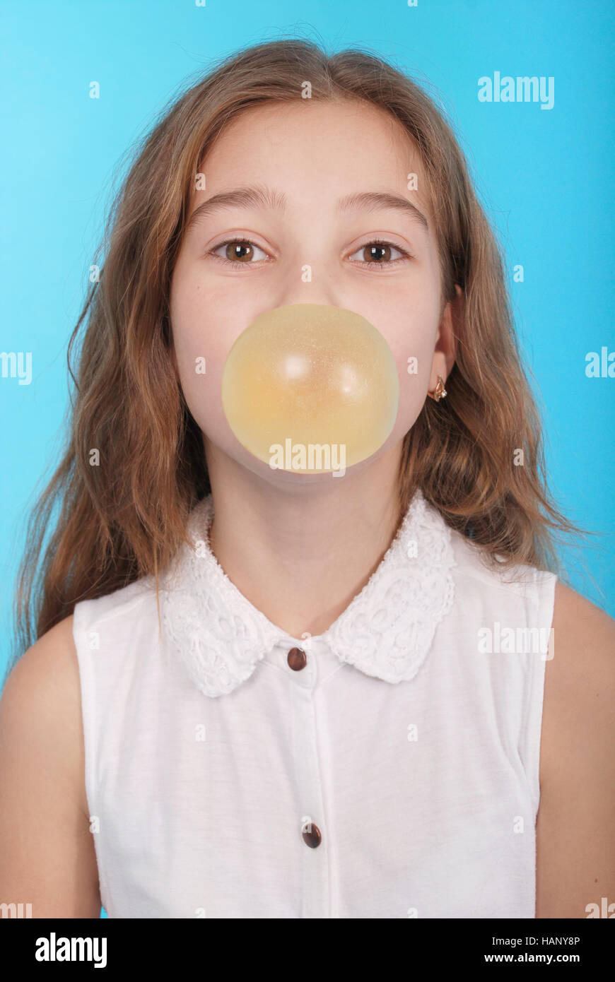 Young girl making a big bubble with a chewing gum isolated on blue