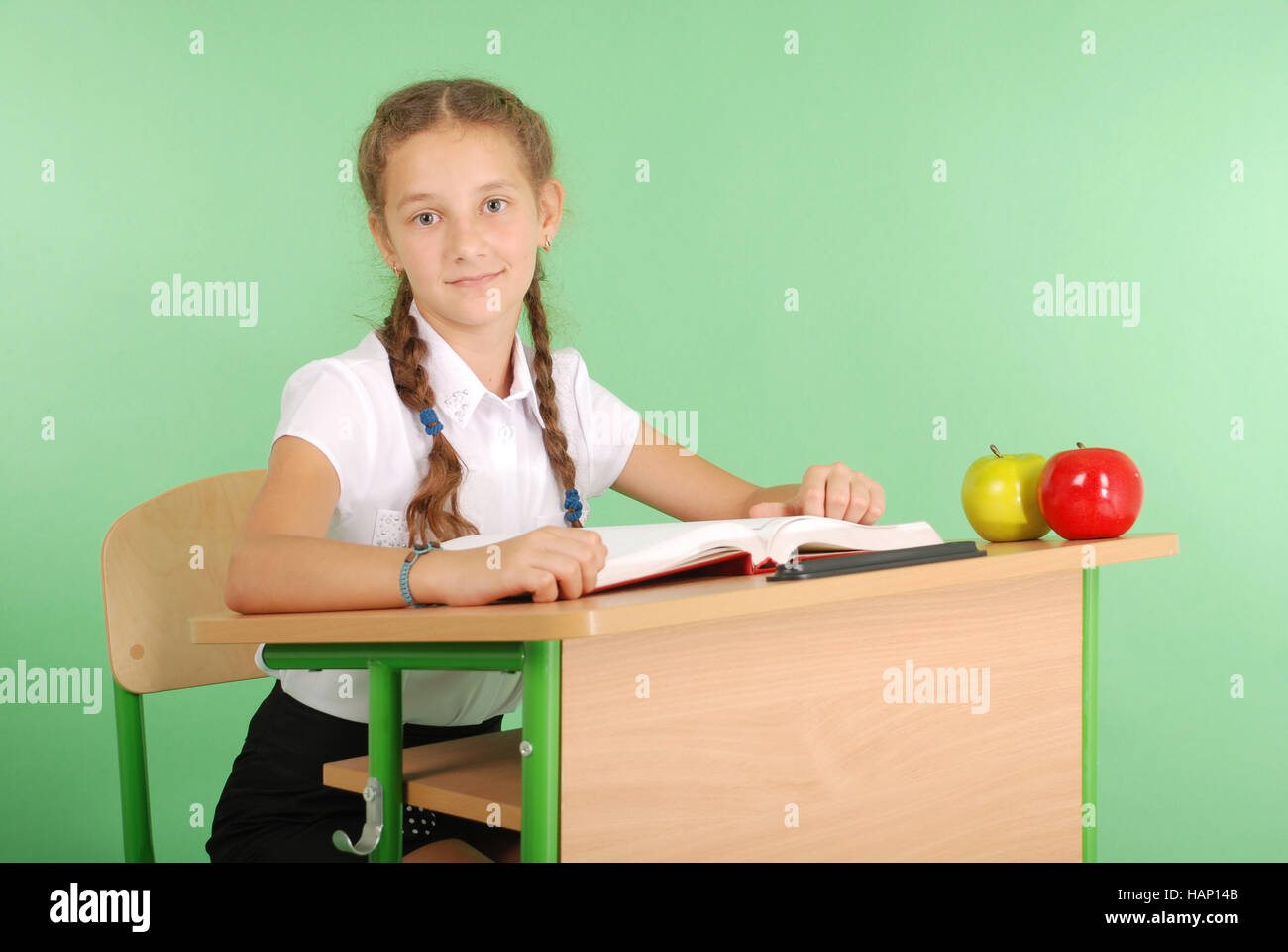 Girl in a school uniform sitting at a desk and reading a book isolated ...
