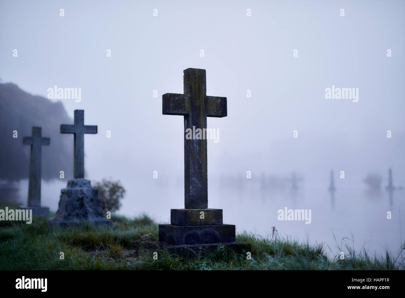 Crosses on gravestones in ethereal flooded foggy cemetery Stock Photo