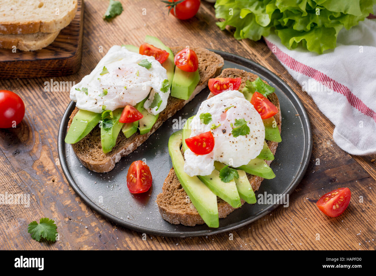 Close up view of delicious poached egg and avocado toasts garnished with chopped parsley. Selective focus Stock Photo