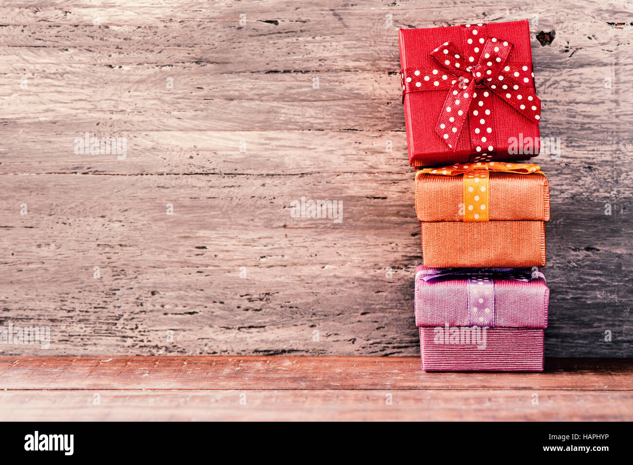 a stack of some cozy gifts wrapped in different papers and tied with ribbons of different colors on a rustic wooden surface, with a negative space Stock Photo