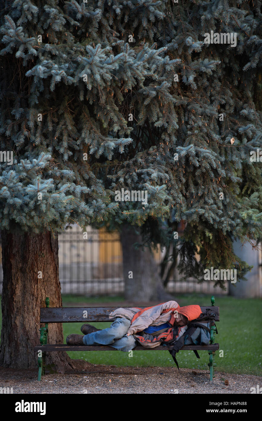 Homeless man sleeping on a bench within the grounds of The Basilica Eger Erlau or Egri Bazilika, Hungary, Europe Stock Photo