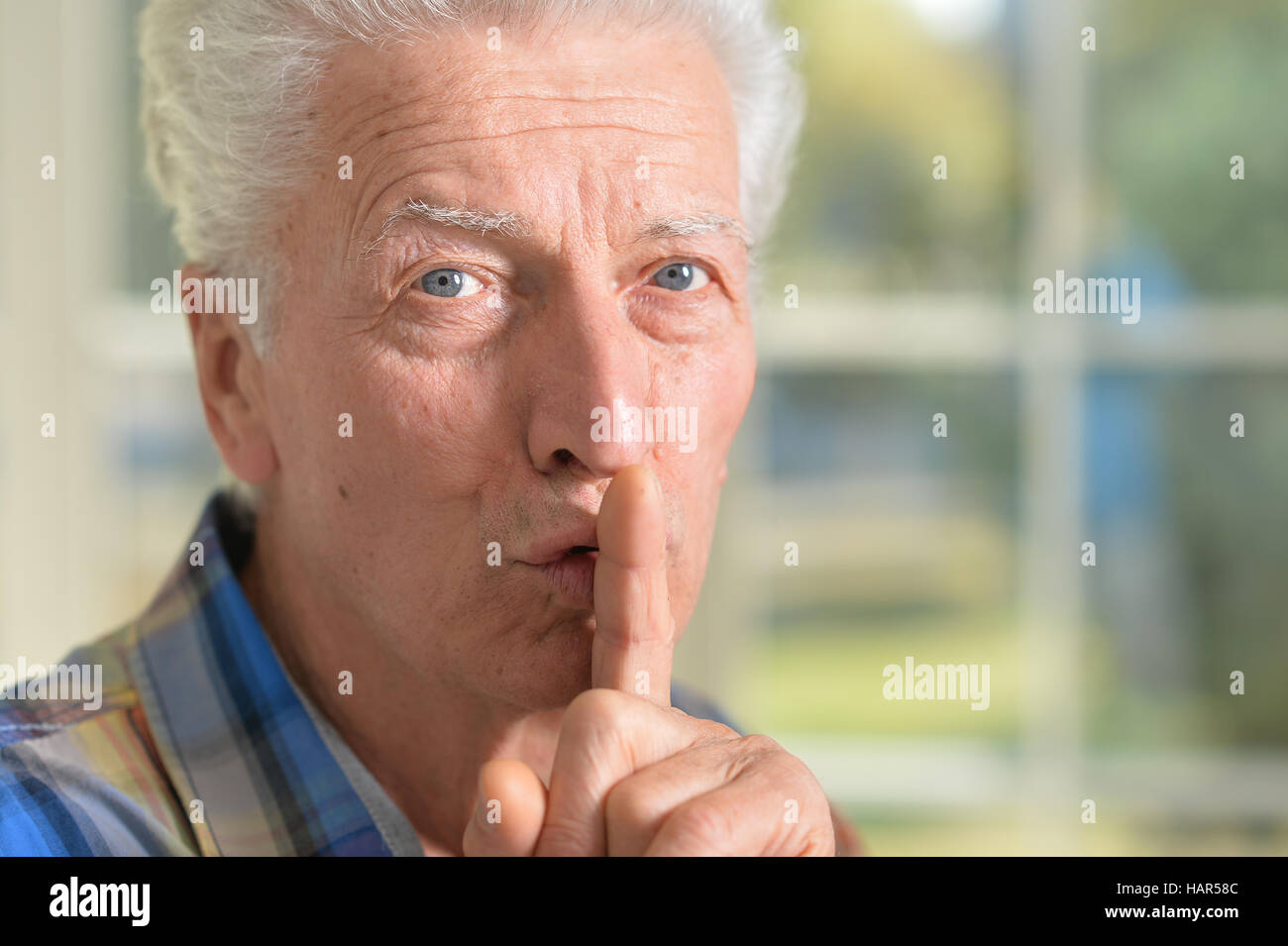 Senior man presses his finger on mouth Stock Photo