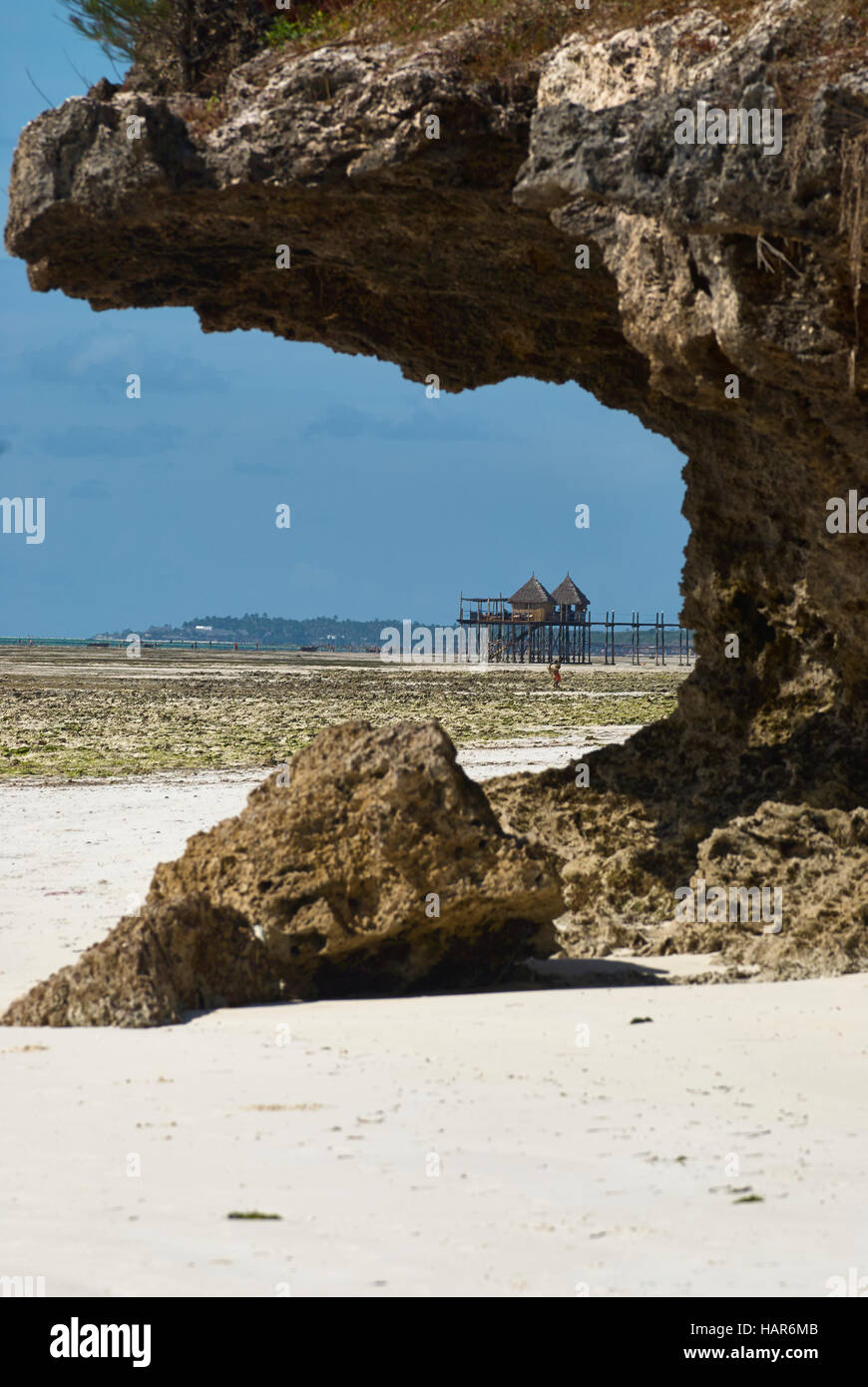 Beach view through a coral rock cliff with a jetty and restaurant on poles Stock Photo