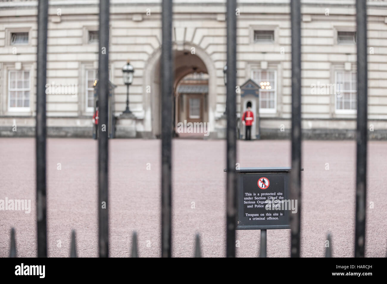 London info panel about illegal trespass. Queen's guards of Buckingham Palace view through the fence Stock Photo