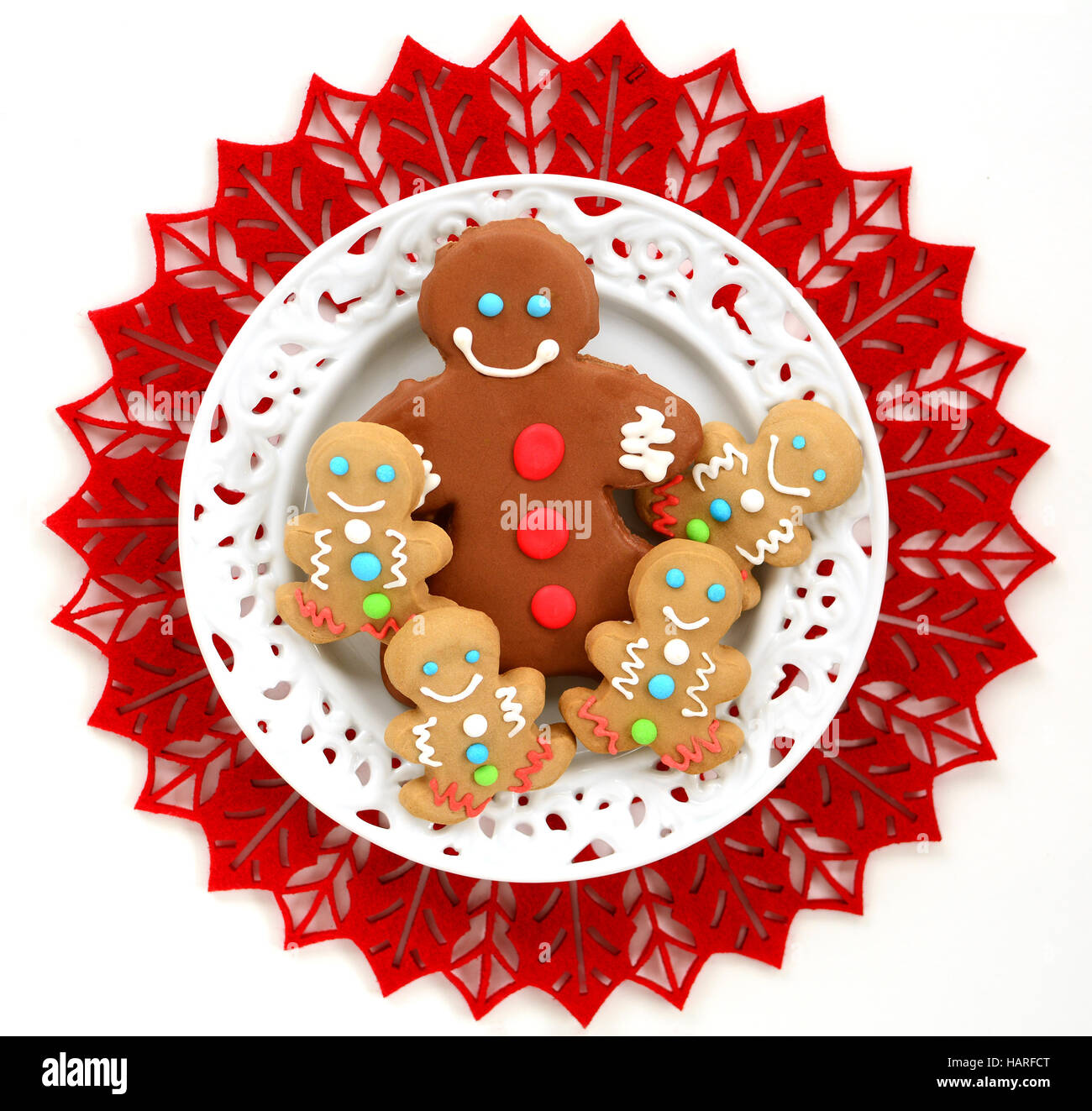 Cute little decorated gingerbread men on white plate and red felt mat in square format from overhead Stock Photo