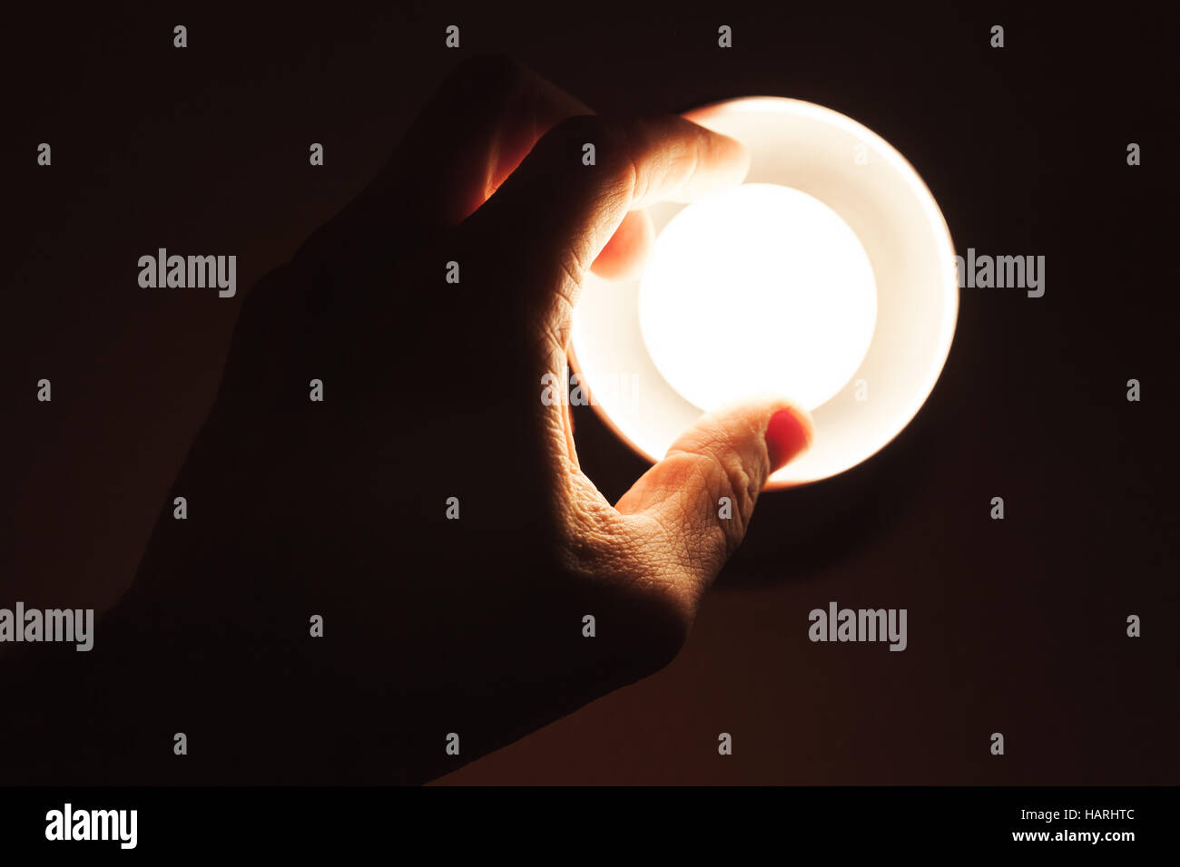 Male hand turning on small tungsten lamp in metal lampshade over black background, closeup photo Stock Photo