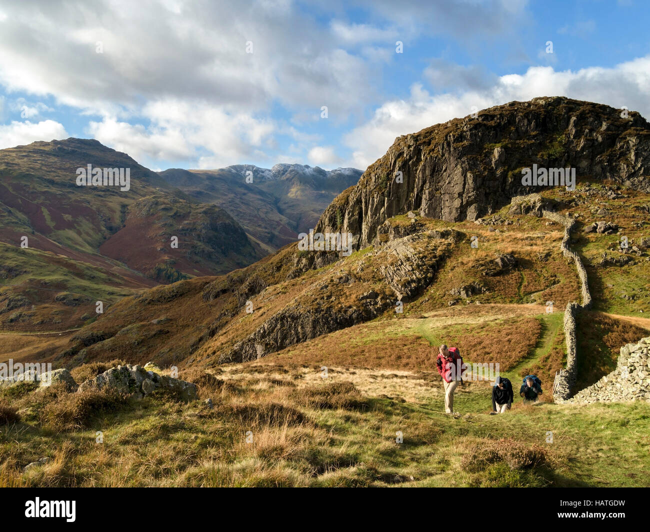 Walkers and dry stone wall on Lingmoor Fell with Side Pike (right) and Pike O'Blisco (left) and Crinkle Crags beyond, Cumbria, UK Stock Photo