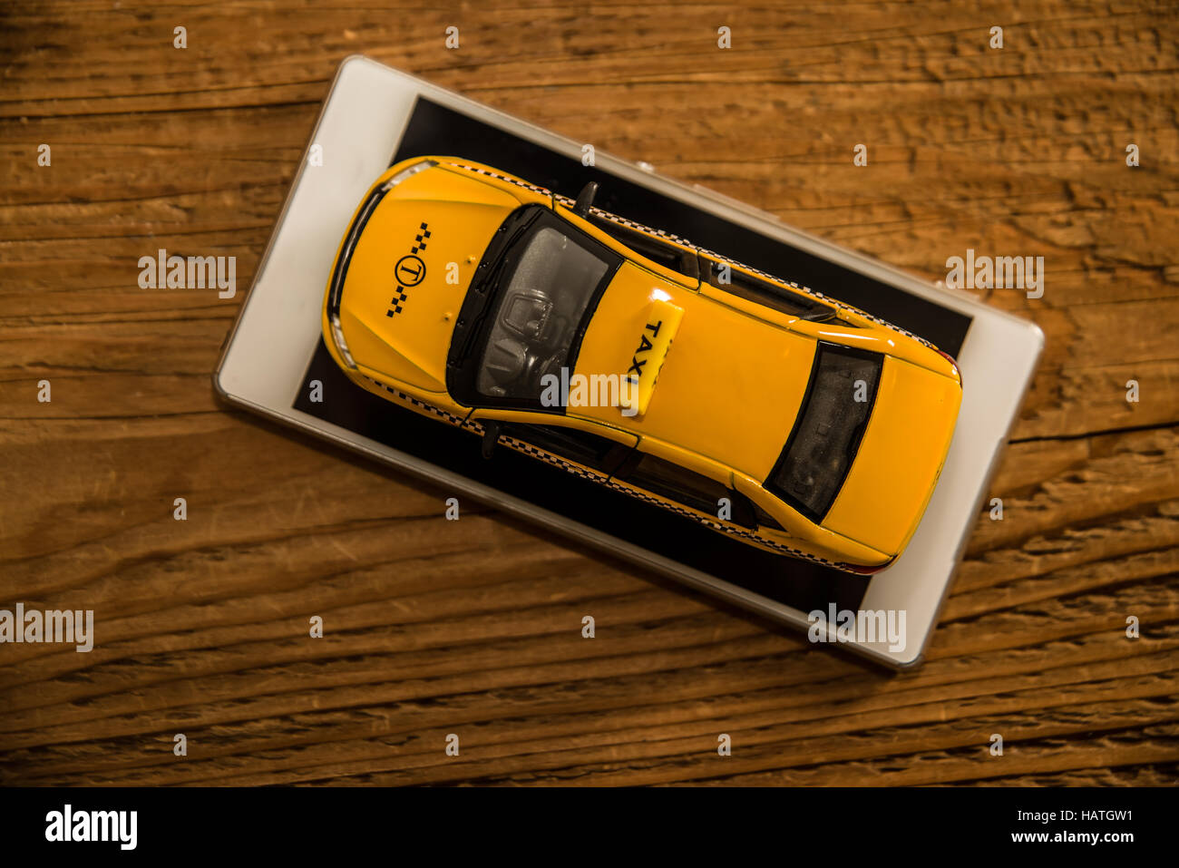 up view. yellow Taxi car - metal model stand on screen of white Smartphone. mobile phone lie on wooden table. empty copy space for inscription Stock Photo