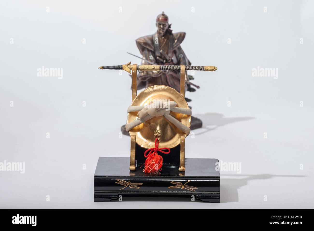 Miniature Japanese Kabuto helmet and sword in front of statue of Samurai Stock Photo