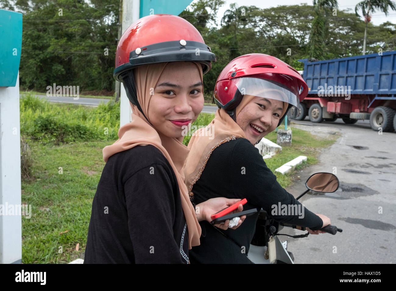 Two identically dressed Muslim girls, sit on a motor scooter in Mukah, Mukah Division, Sarawak, Malaysia Stock Photo