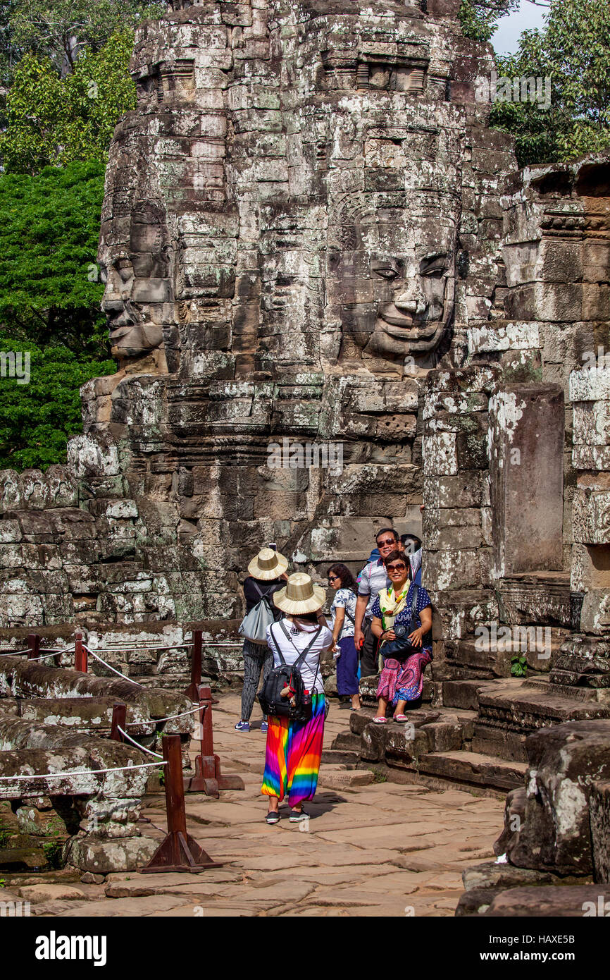 Ancient sandstone faces at Prasat Bayon in Angkor Thom stare down at tourists visiting the temple complex in Cambodia. Stock Photo