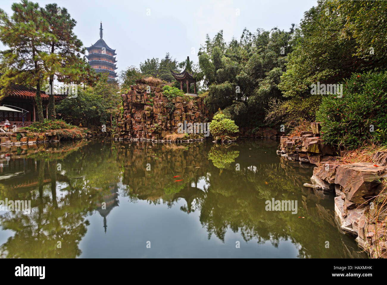 Picturesque traditional chinese garden with calm pond, red carp fish, tall pagoda, pavilions and trees in Suzhou. Stock Photo