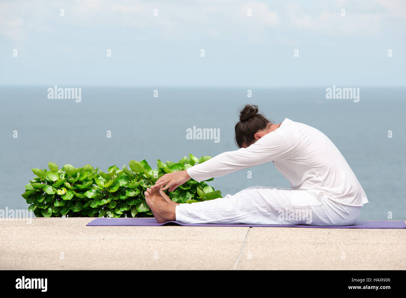 Caucasian man in white clothes meditating yoga on the sea shore pier Stock Photo