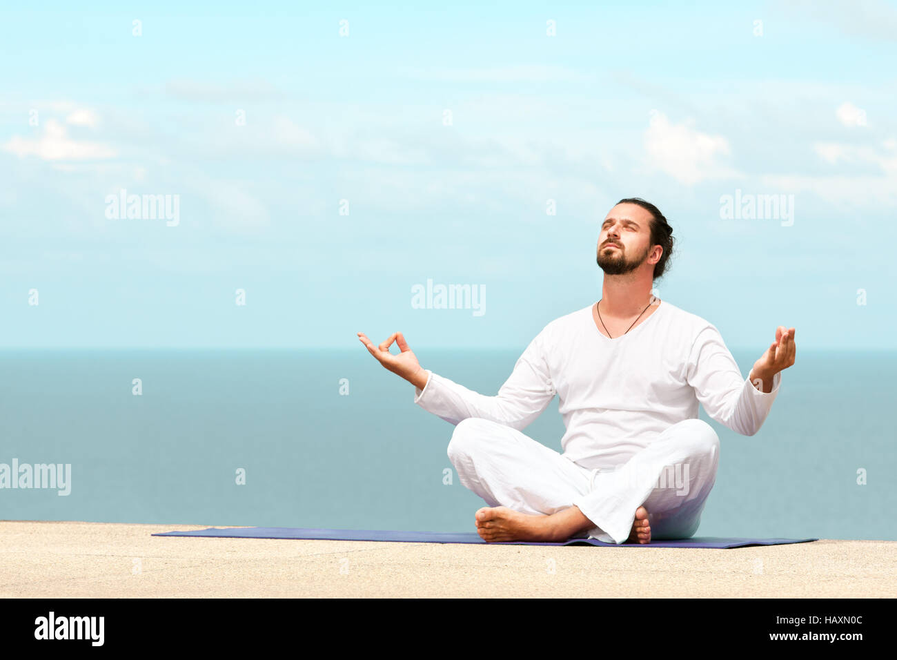 Caucasian man in white clothes meditating yoga on the sea shore pier Stock Photo