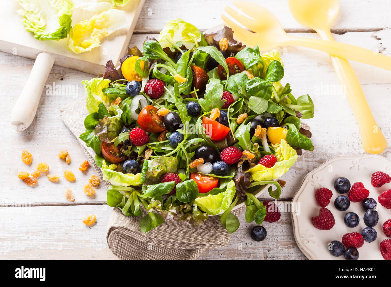 Fresh green salad with raspberries and blueberries on a white wooden table. Stock Photo