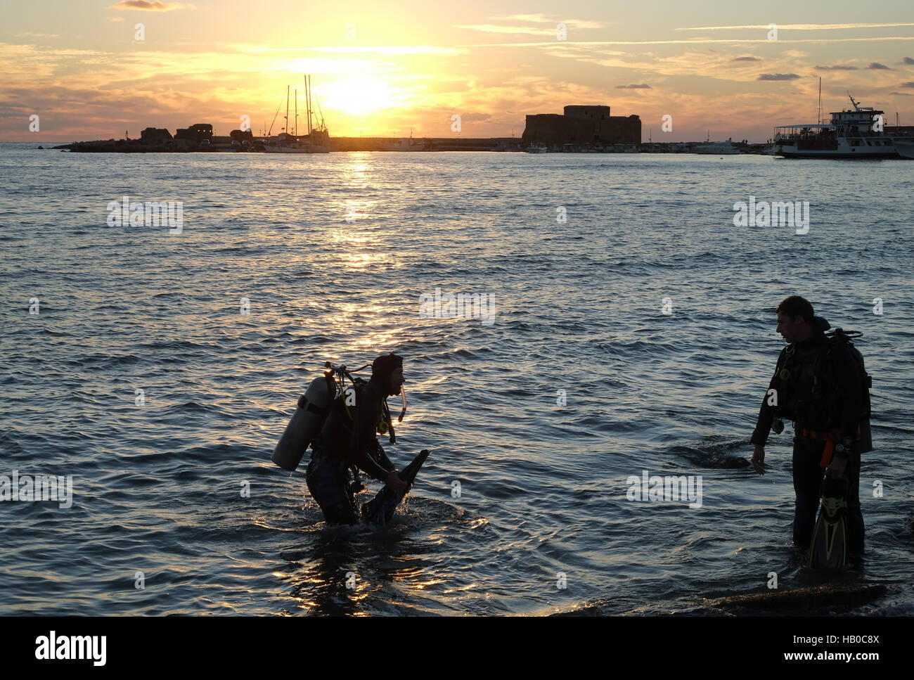 Cydive diving instructor and pupil leave the water at sunset after a diving session on the waterfront in Paphos Harbour. Stock Photo