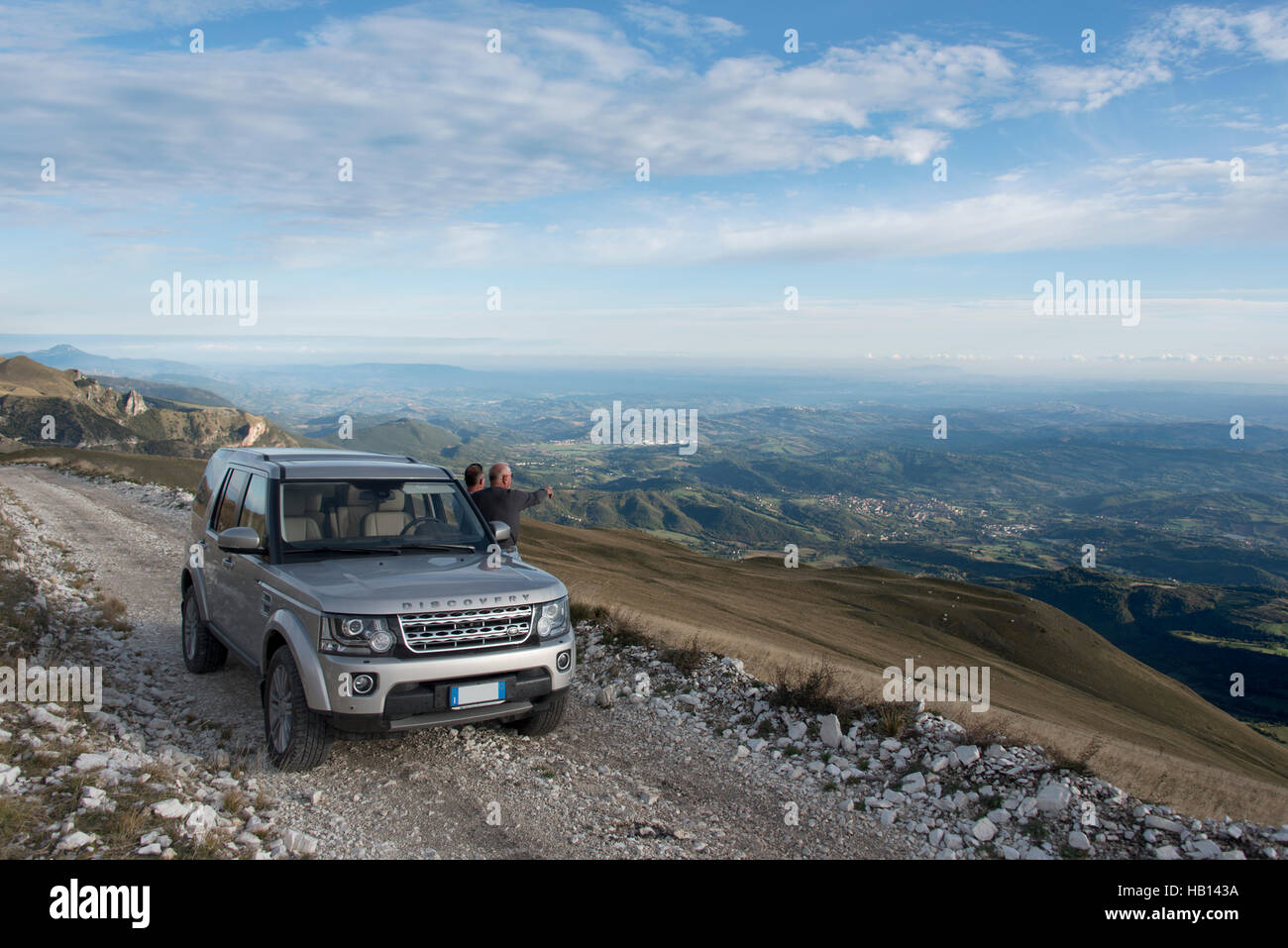 Two men stood next to a new Land Rover Discovery 4 looking out over the Marche landscape in Italy Stock Photo