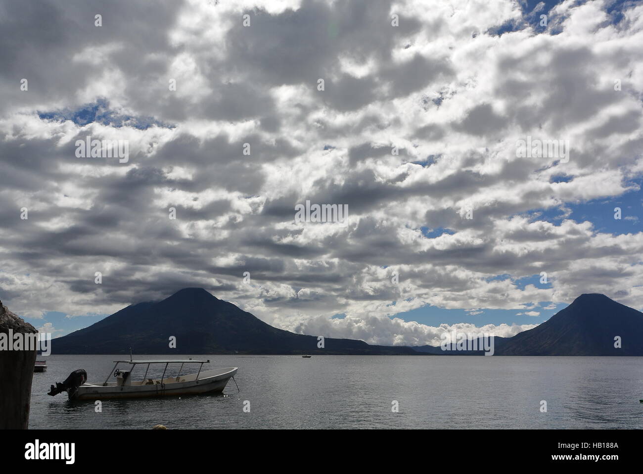 Lago Atitlan, Guatemala. Dock and boats on left foreground, view over Lago Atitlan to volcanos in background, dramatic clouds Stock Photo