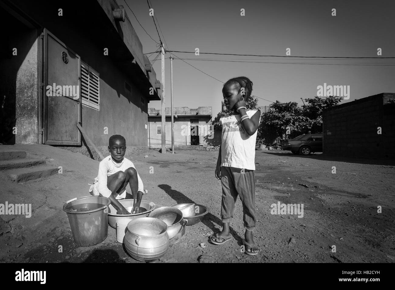 BAMAKO, MALI, DEC 23: Two African native young girls washing the dishes outside the house in the residential district of Bamako. Mali 2010. Black and  Stock Photo