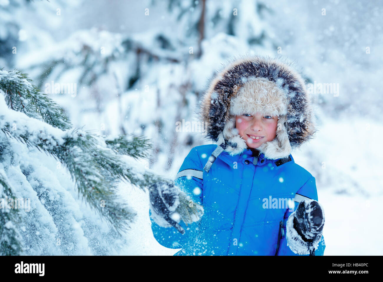 Cute little boy wearing warm clothes playing on winter forest on beautiful winter snowy day Stock Photo