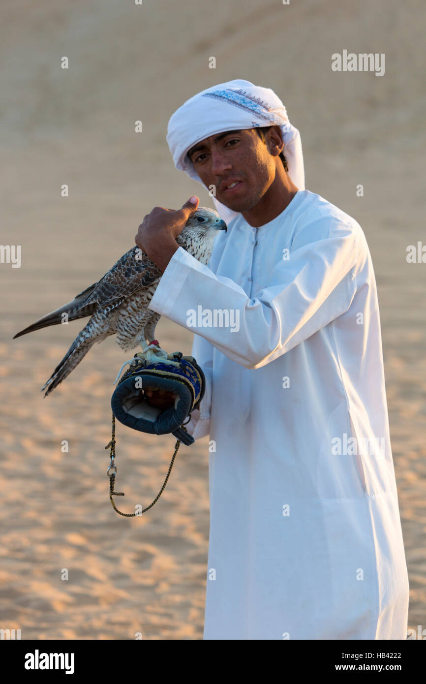 Young arab man holding a hawk in the desert near Dubai, UAE Stock Photo