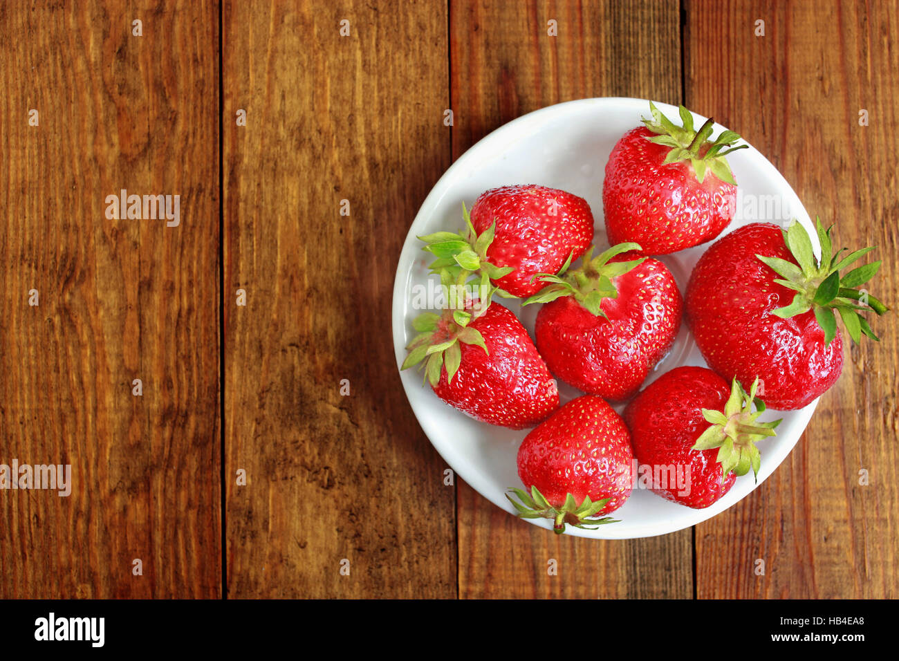 ripe red strawberries on the white plate on the brown background Stock Photo