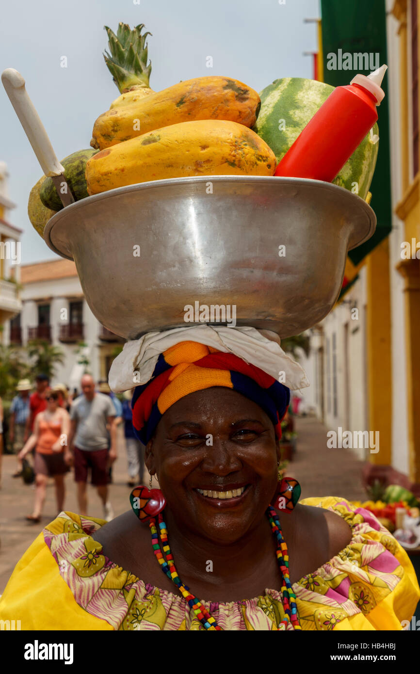Colombian woman smiling as she carries a bowl of fruit on her head Stock Photo