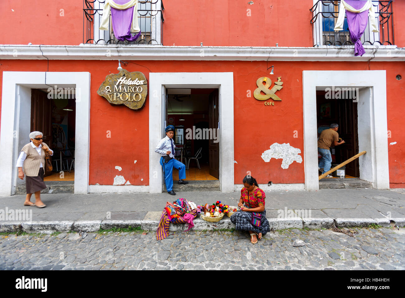 Security guard an the door of the Marco Polo bar and restaurant. Woman sitting on the kerb selling souvenirs Antigua Guatemala. Stock Photo