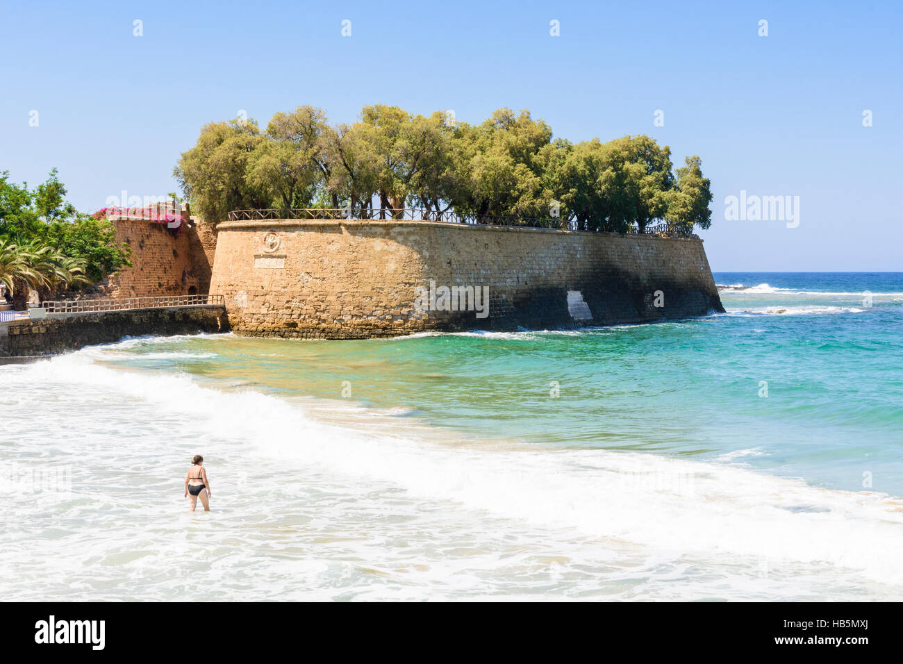 A woman walks into the sea near the Sabbionara Rampart part of the Venetian fortifications surrounding old Chania, Crete, Greece Stock Photo