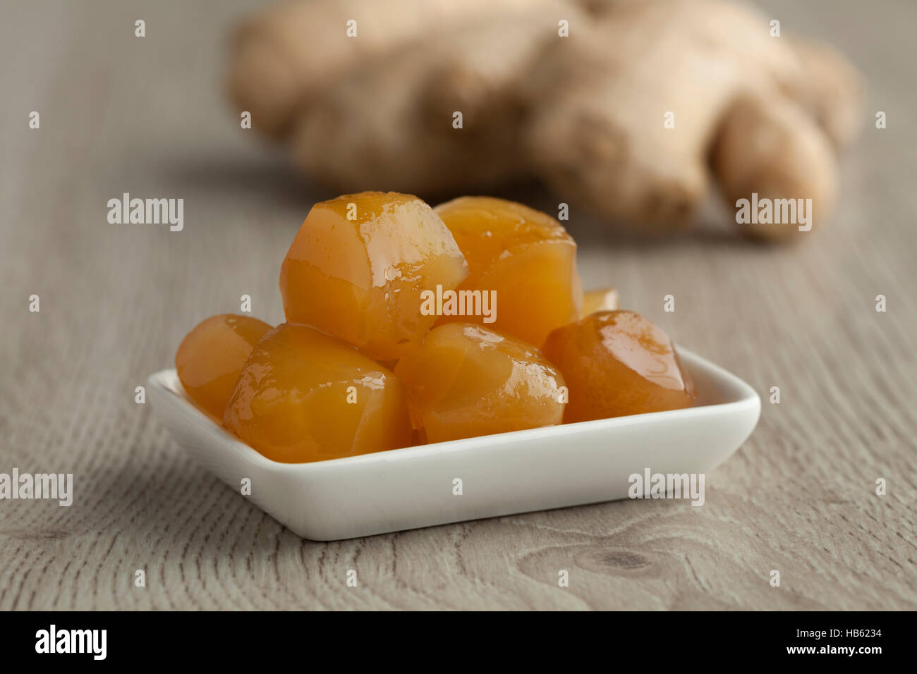 Dish with stem ginger in syrup  with fresh gingerroot in the background Stock Photo
