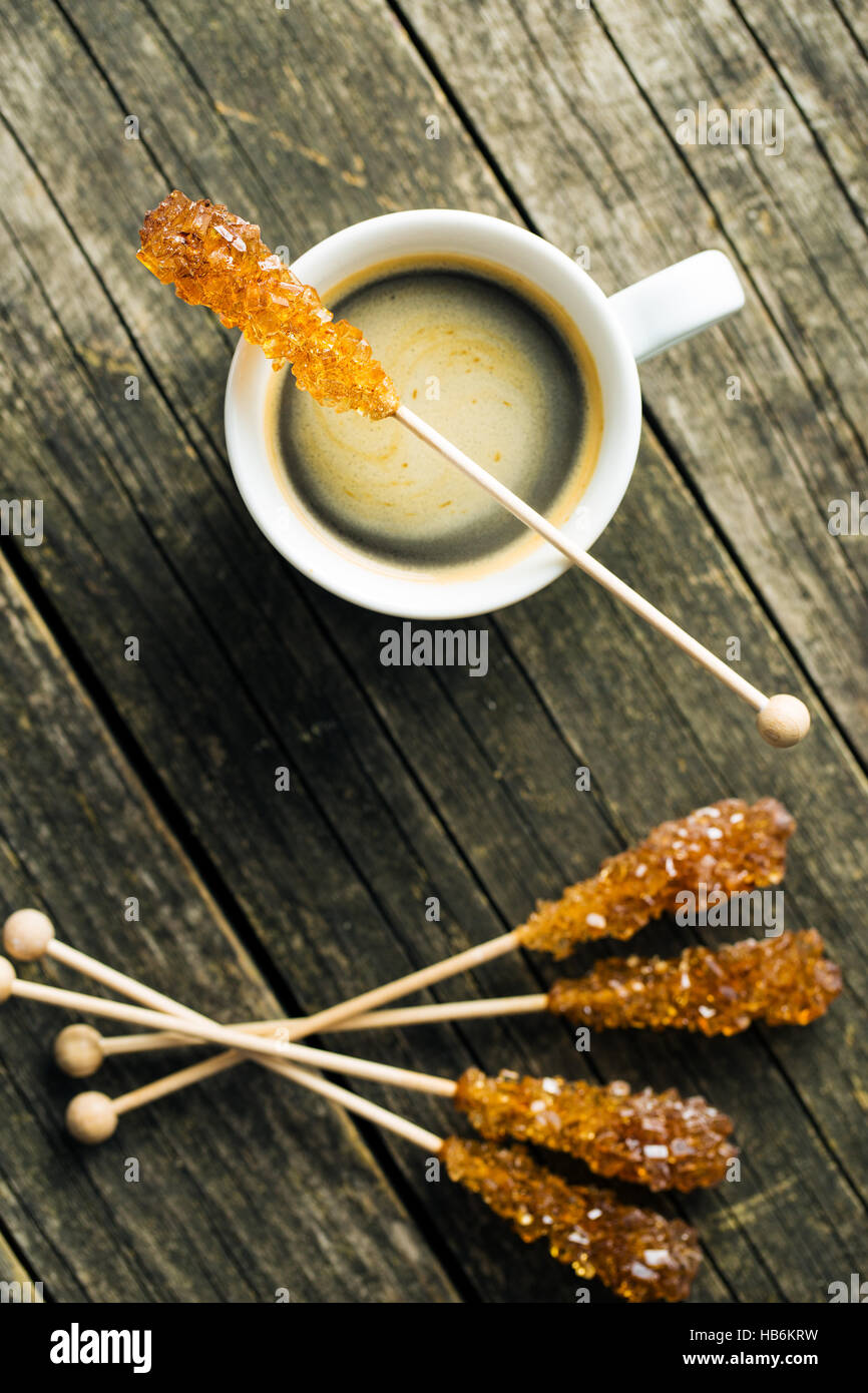 Brown amber sugar crystal on wooden stick and coffee cup. Top view. Stock Photo