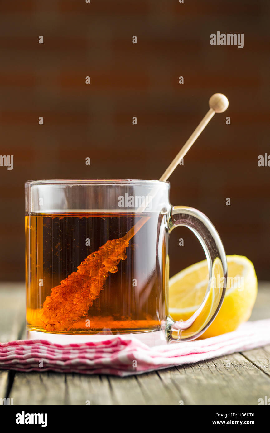 Tea cup with sugar crystal on wooden stick on old wooden table. Stock Photo