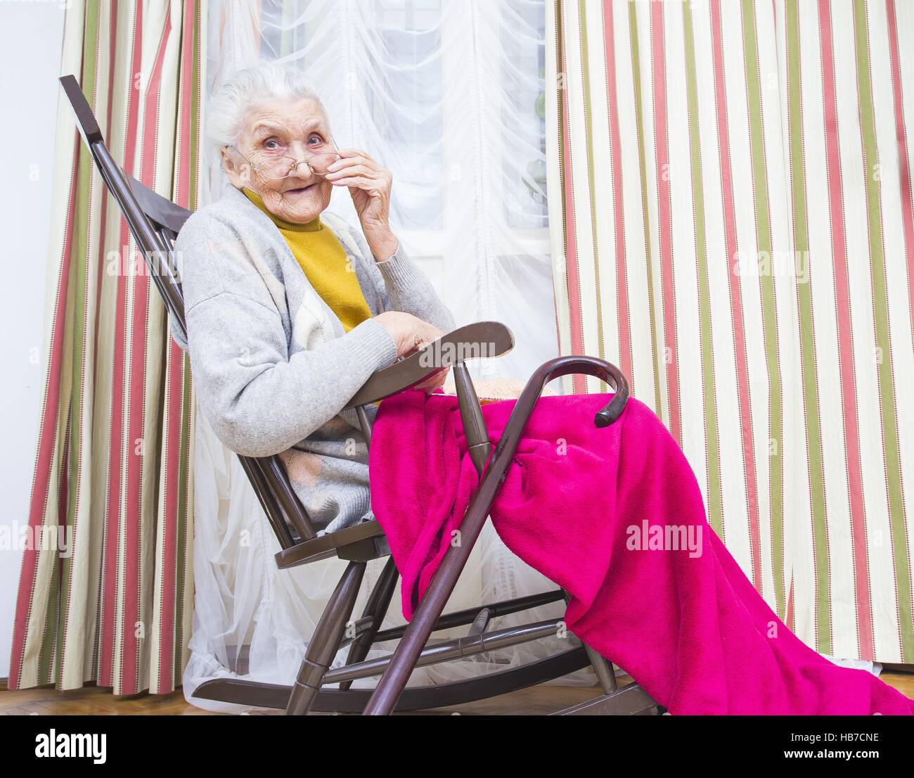 Elderly lady with a walking stick sitting in a chair. Stock Photo