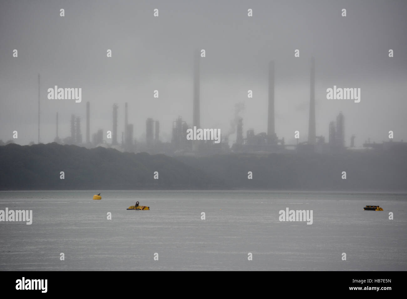 Yellow mooring buoys standing out of a grey sea with Pembroke Refinery almost silhouetted in the grey mist Stock Photo