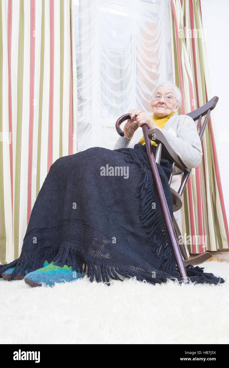 Elderly lady with a walking stick sitting in a chair. Stock Photo