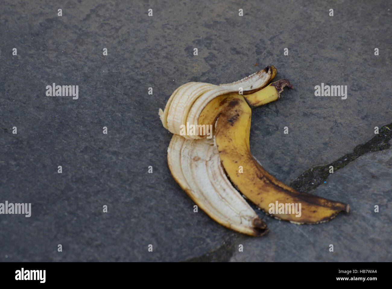 Discarded banana skin lying on public pathway creating a danger of slipping and falling Stock Photo