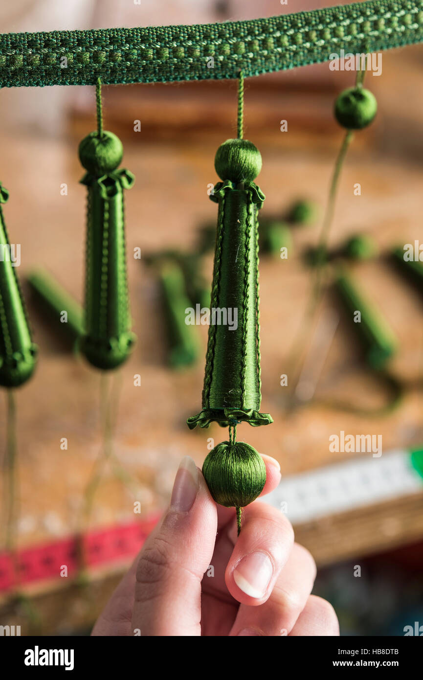 Passementerie maker, hand making green Empire fringe consisting of two spheres and long wooden base wrapped with silk threads, Stock Photo