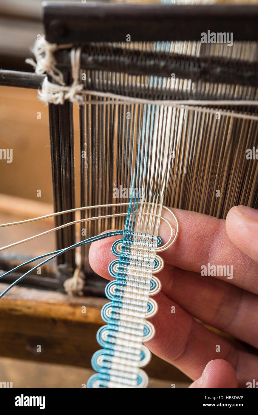 Passementerie maker, hand holding blue and beige gimp, weaving crepine or woven border, part of finished crepine on handloom Stock Photo