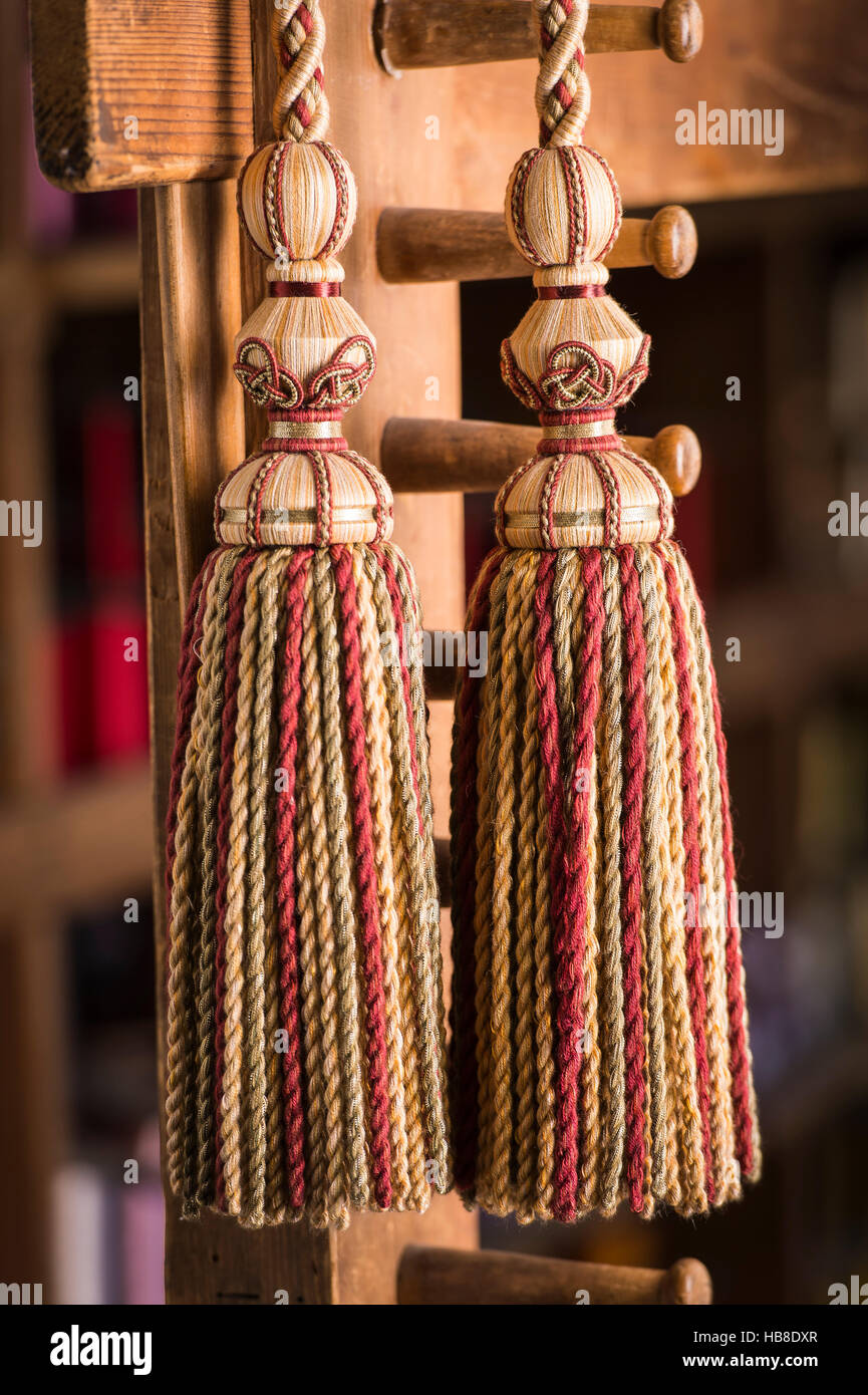 Passementerie, two cord tassels with matching cord, beige and brown, assembled on three wooden bases hanging on wooden rack Stock Photo