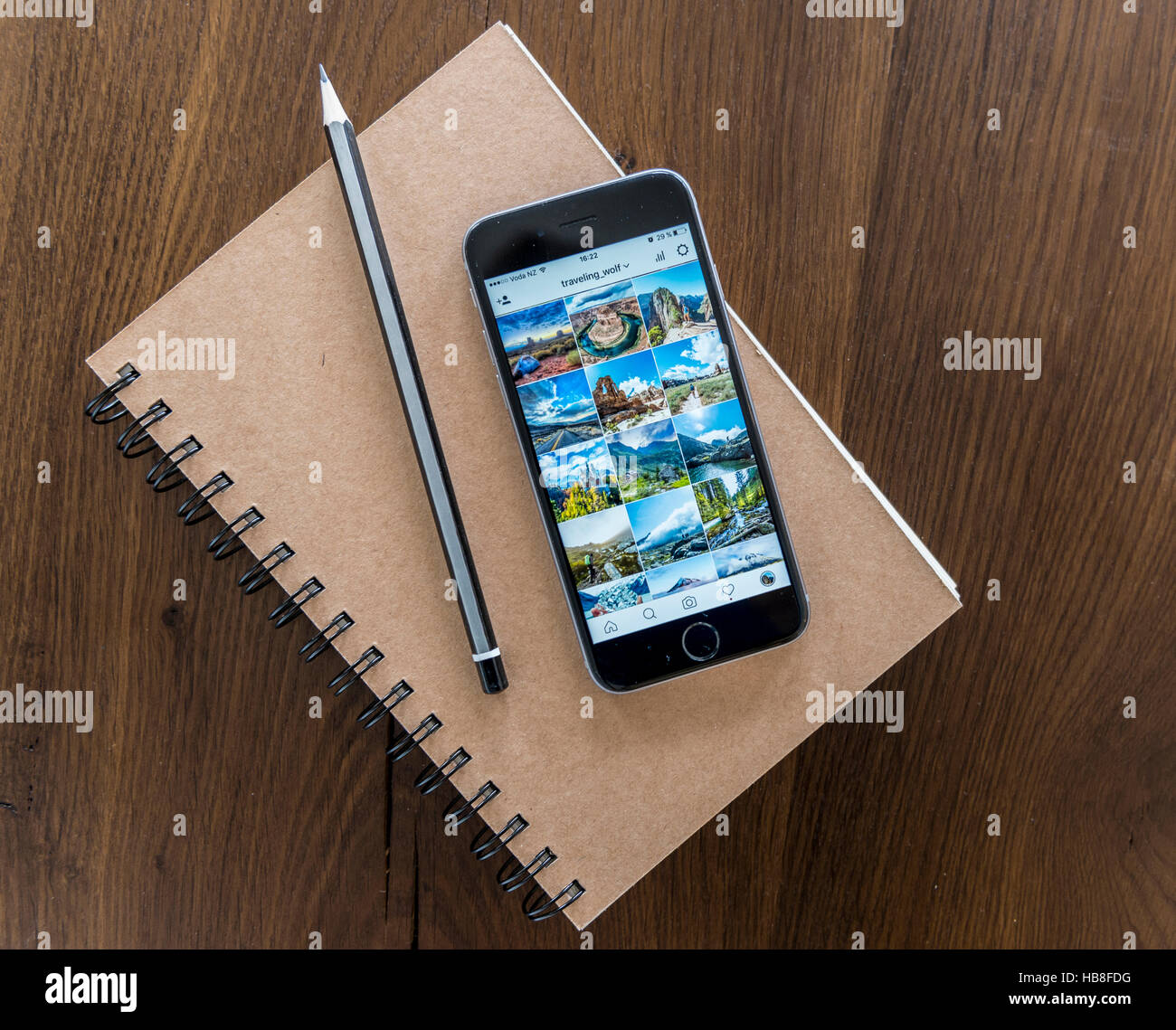 Instagram picture gallery displayed on smartphone screen, notebook and pen on a wooden table Stock Photo
