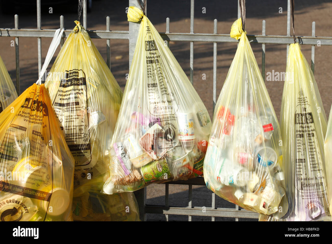 Yellow bags with plastic waste, hanging on garden fence, waste