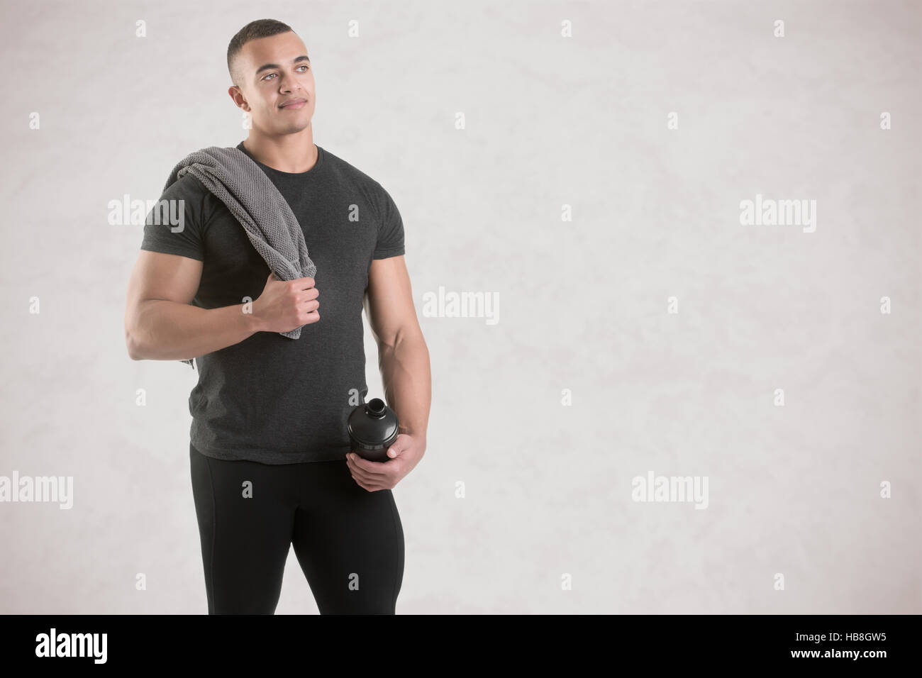 Man holding a protein shake after a workout in the gym, isolated in grey Stock Photo