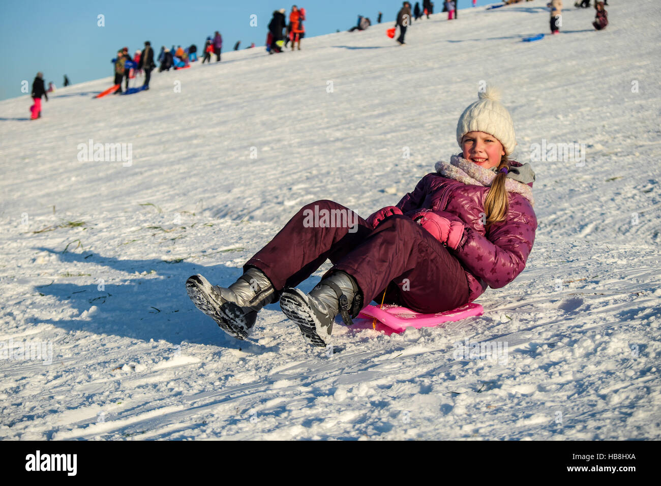 Active young cute girl sledding down the hill on sunny winter day Stock