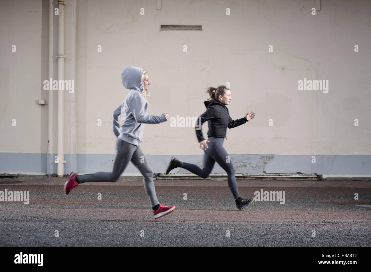 Two female runner friends running on urban road Stock Photo
