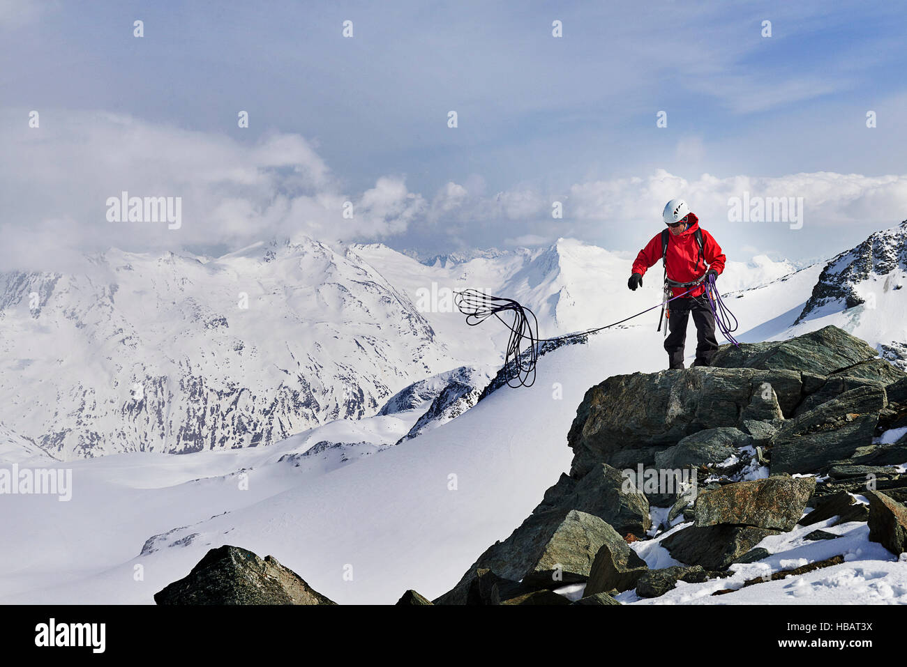 Man on top of snow covered mountain throwing climbing rope, Saas Fee, Switzerland Stock Photo